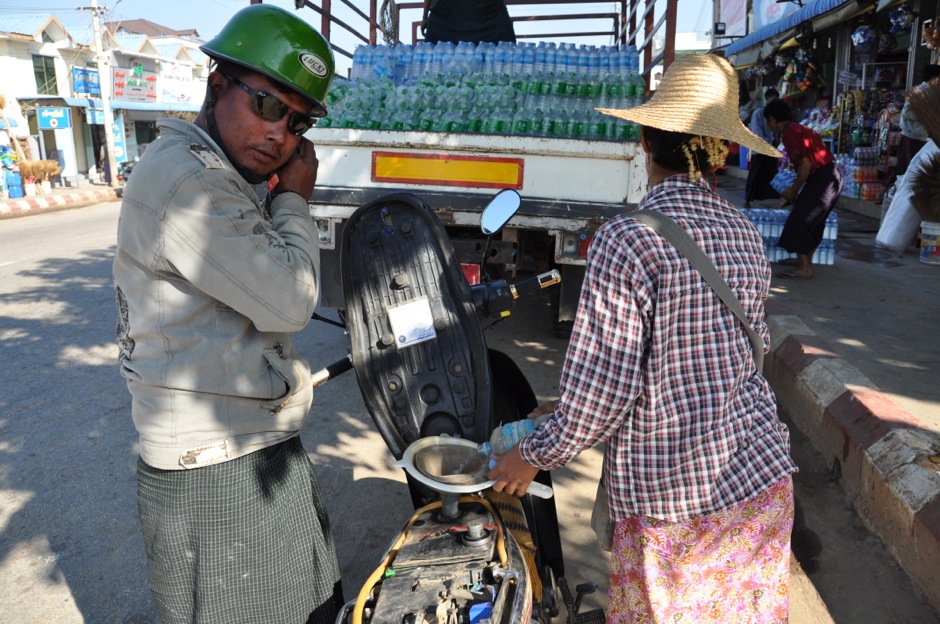 8. BIRMA, Nay Pyi Taw. Powrót do normalności czyli smak Birmy, w tym jakże niebirmańskim mieście. Mototaksówka, ludzie w longyi i paliwo z plastikowej butelki. W tle kawałek typowego dla Birmy bazaru. (fot. Marek Lenarcik) Mototaksówka