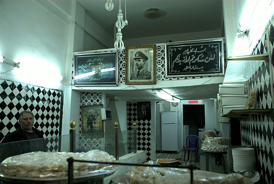 14. JORDANIA, Amman, grudzień 2013. Monarchowie jordańscy są wszechobecni - podobizny ojca miłościwie panującego Abd Allaha II, króla Husejna I, spotkać można głównie w najstarszych zakładach usługowych, sklepach, piekarniach, restauracjach czy zakładach krawieckich. Tu wnętrze cukierni przy ulicy Króla Fajsala - w centralnym miejscu powieszono zdjęcie Husajna z czasów gdy uczył się w brytyjskiej akademii wojskowej Sandhurst. (Fot. Norbert Skrzyński) Portrety króla Jordanii wiszą wszędzie - foto