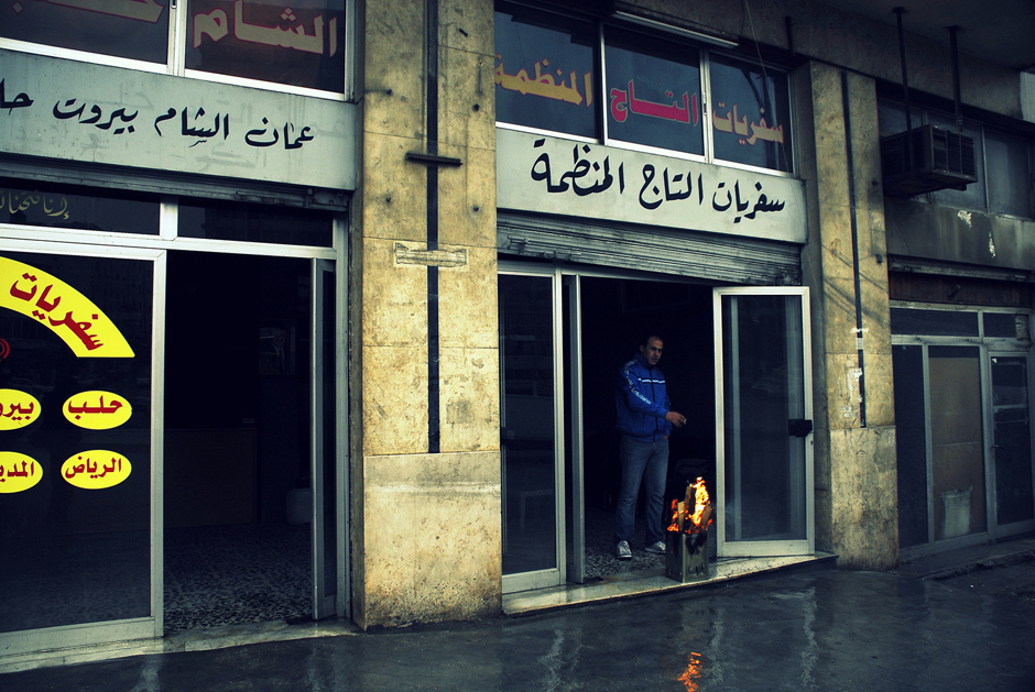 16. JORDANIA, Amman, grudzień 2013. Aura w Ammanie może zaskakiwać. Nie tylko ammańczyków. Plac Abdali w czwartki i piątki staje się kolorowym bazarem. Jeszcze kilka lat temu był sporym dworcem autobusowym. Odjeżdżały stąd autobusy m.in. do Damaszku, Bejrutu czy Stambułu. Świadczą o tym naklejone na szyby reklamy promujące wyjazdy do Libanu czy Syrii. Gdy aura nie sprzyja, sprzedawcy wycieczek ogrzewają się i suszą przy przenośnych paleniskach stawianych tuż przy wejściu do biur i sklepów. (Fot. Norbert Skrzyński) Amman - zdjęcia z podróży do Jordanii
